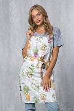 Woman wearing the white herb pots print apron with tan contrasting straps